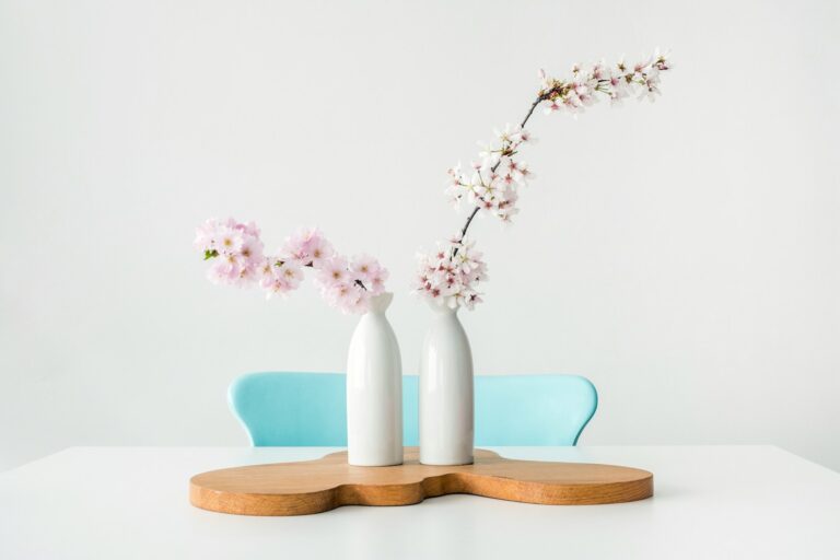 two pink petaled flowers in white vases on brown wooden surface